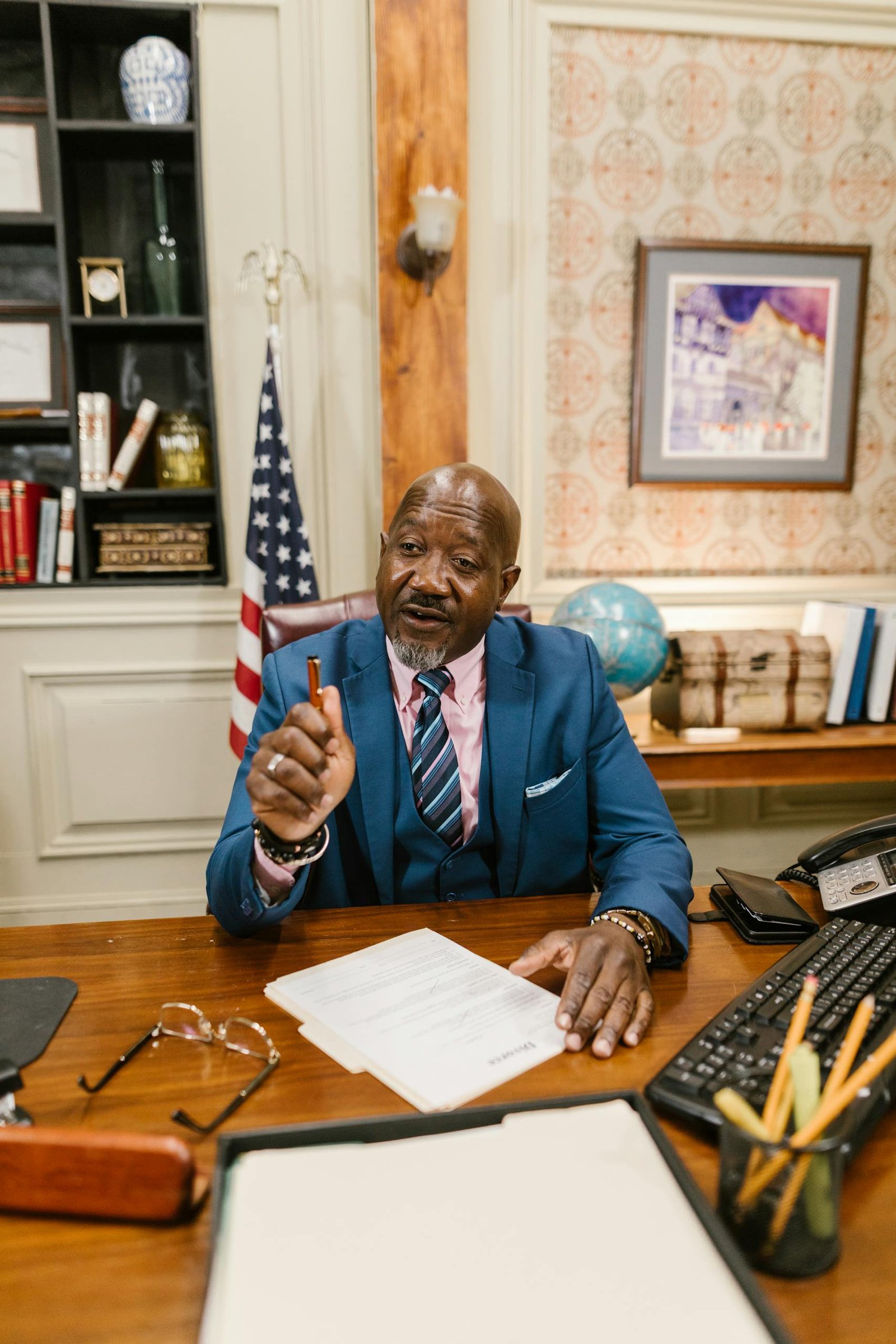 Mature male professional reviewing documents in a well-decorated office with bookshelves and US flag.